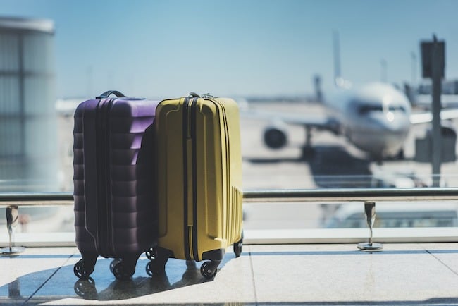 Two suitcases in the airport departure lounge, airplane in the blurred background, summer vacation concept, traveler suitcases in airport terminal waiting area, empty hall interior with large windows, focus on suitcases