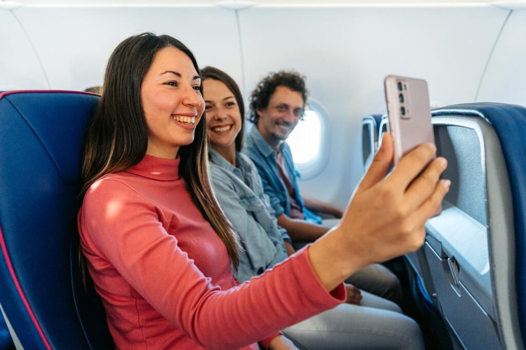 Passengers smiling and taking a selfie together while seated inside an airplane cabin