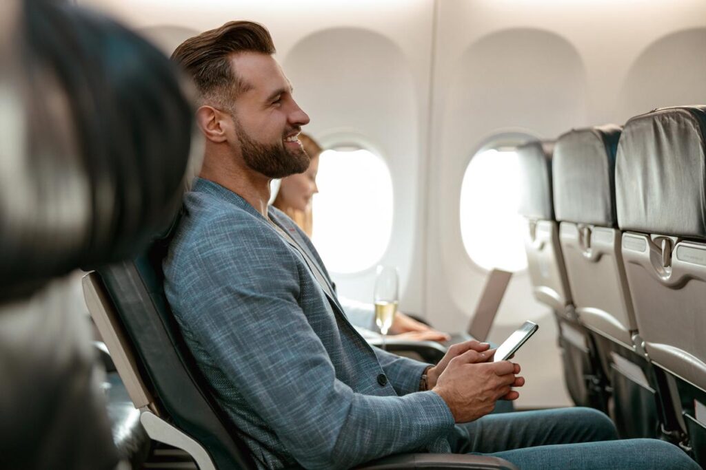 Male passenger relaxing with a phone in airplane seat during flight.