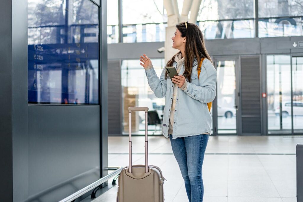 A woman traveler with luggage checking the flight information board at the airport.