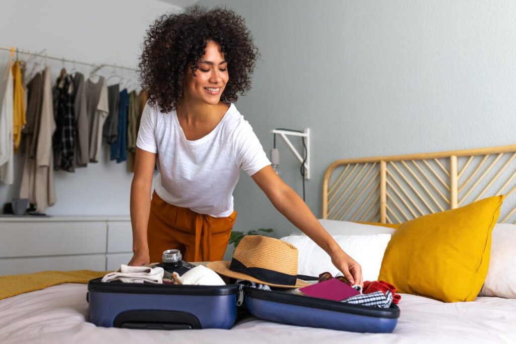 Woman packing clothes and travel essentials into a suitcase on her bed