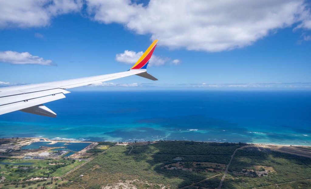 View of airplane wing flying over blue ocean and tropical coastline