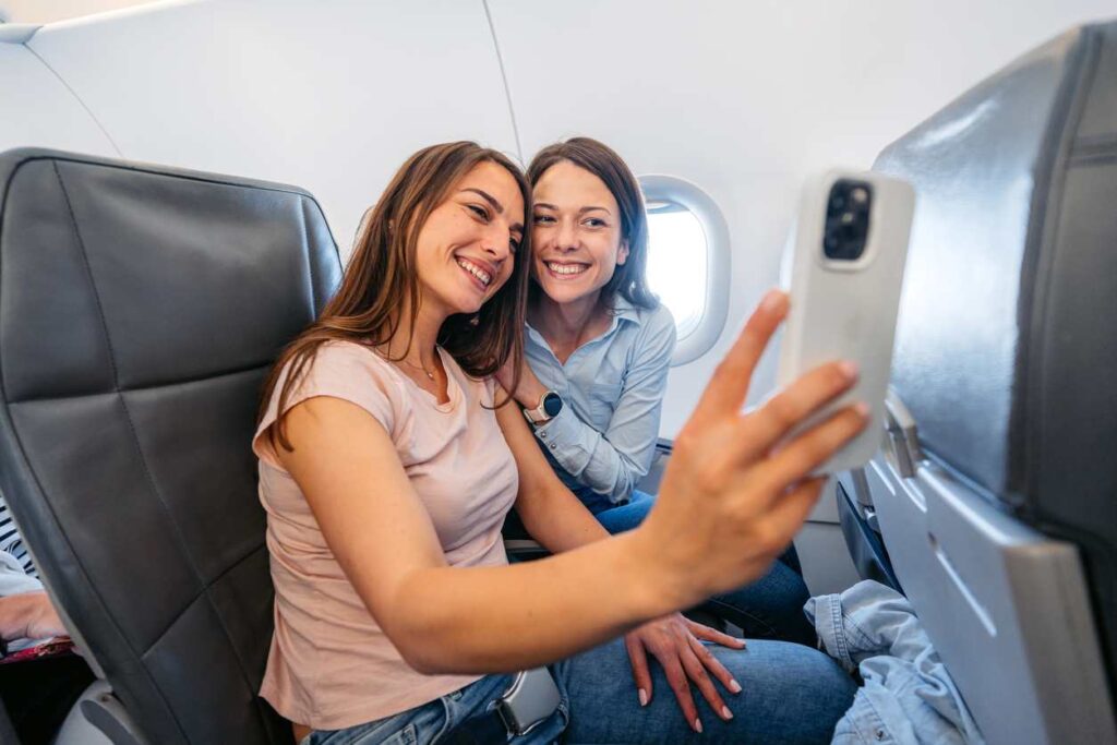 Two friends taking a selfie while sitting on an airplane