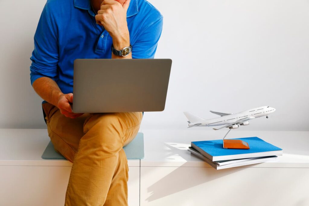 Man using a laptop to book flights online with a model airplane and travel documents on the desk.