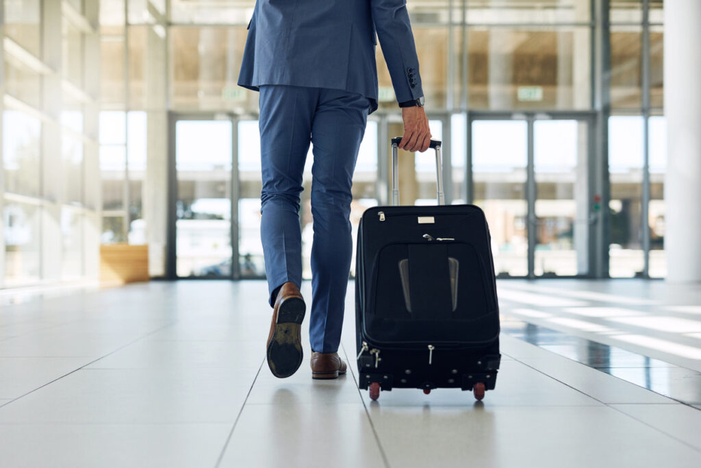 Business traveler walking through an airport with a rolling suitcase, representing how business credit card spending can earn rewards points for free or discounted travel.