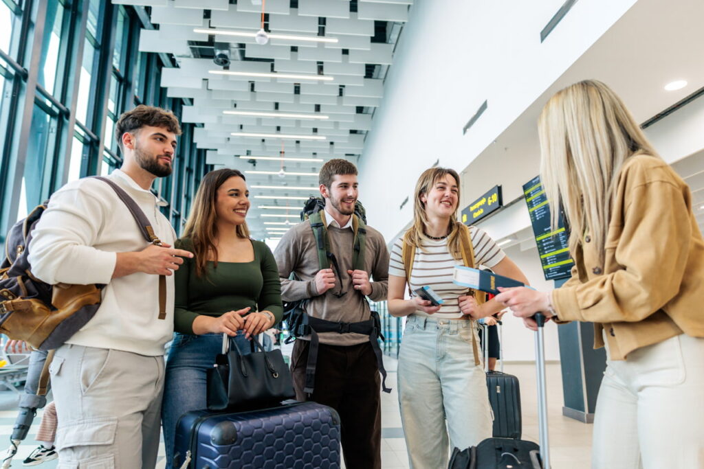 Group of travelers with luggage speaking with an airport staff member in a terminal.